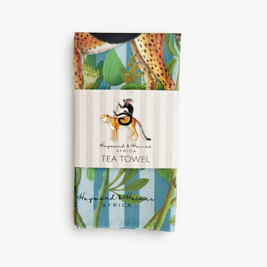 A packaged 100% cotton tea towel with an African safari-themed print, featuring a monkey riding a cheetah,  'Hayward & Haines TEA TOWEL'.