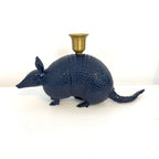 A dark blue armadillo-shaped candle holder with a textured scale finish and a brass cup mounted on its back, set against a plain white background.