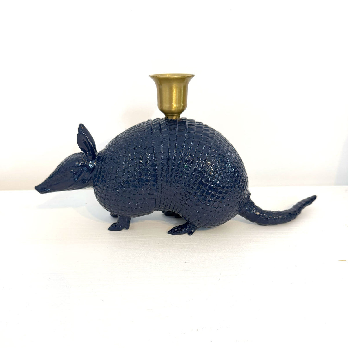 A dark blue armadillo-shaped candle holder with a textured scale finish and a brass cup mounted on its back, set against a plain white background.