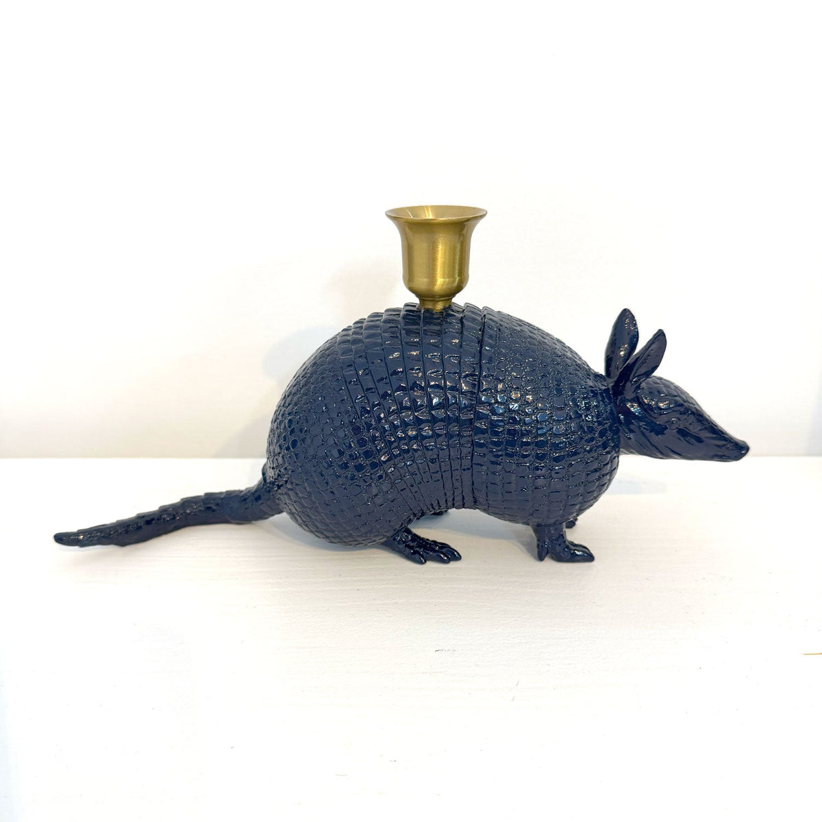 A dark blue armadillo-shaped candle holder with a gold cup on its back, set against a plain white background.
